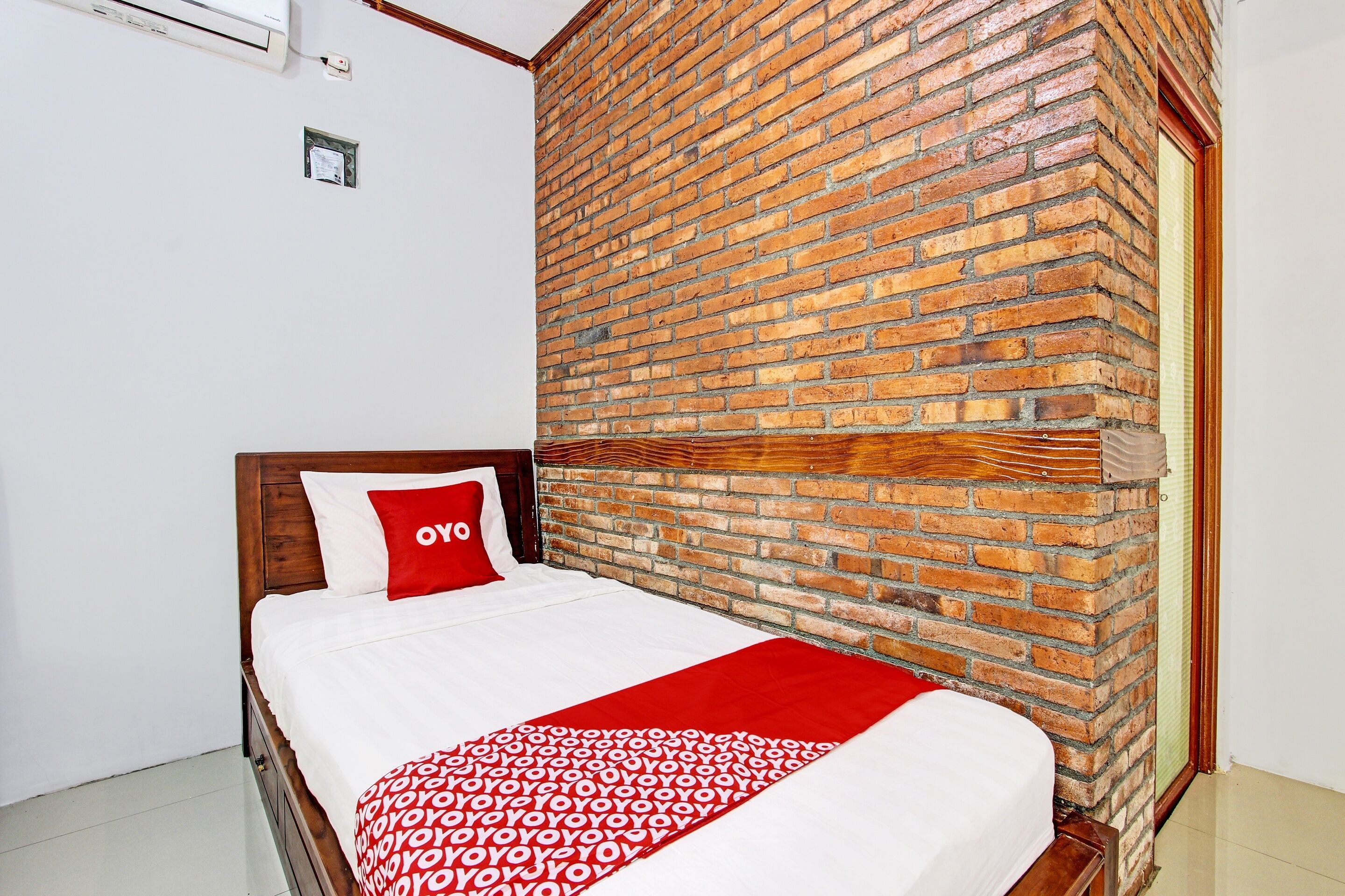 Ein Schlafzimmer mit Backsteinwand, Holz-Kopfstütze und Bett mit weiß-roter Bettdecke.