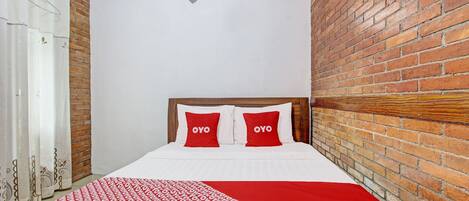 A hotel room with a brick wall, a bed with red and white bedding, and a white air conditioning unit on the wall.