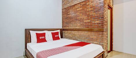Una cama bien tendida con una colcha estampada, una pared de ladrillo decorativa y una unidad de aire acondicionado blanca encima.