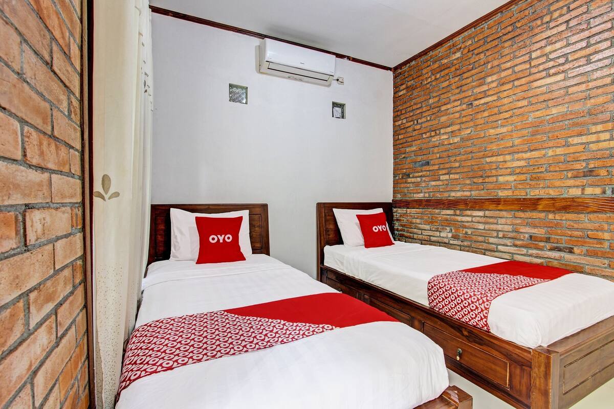 A hotel room with two beds, each with a red and white patterned bedspread, and a brick wall.