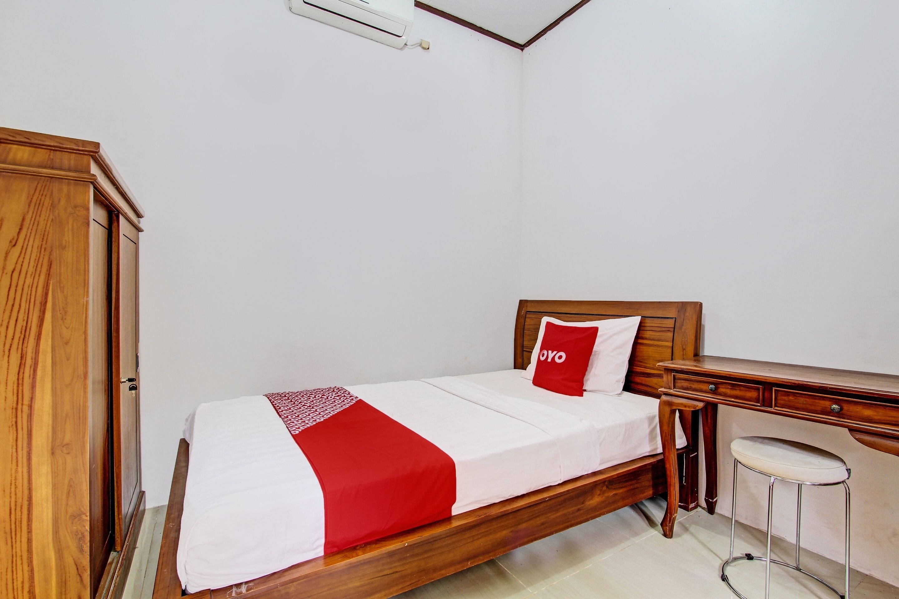 A single bed with a wooden headboard, a red and white bedspread, and a small stool.