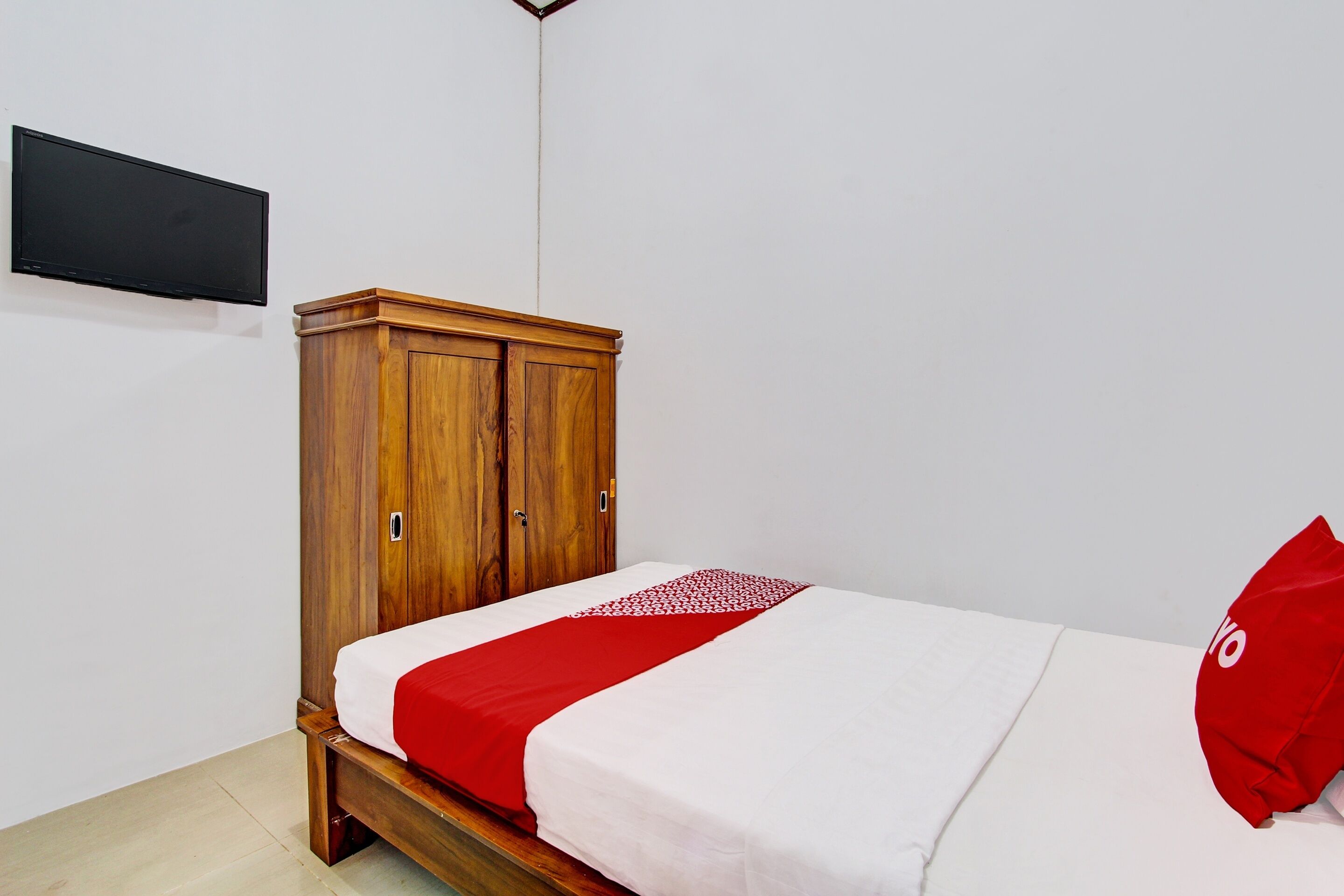 A bedroom with a wooden wardrobe, a bed with white and red bedding, and a red pillow.