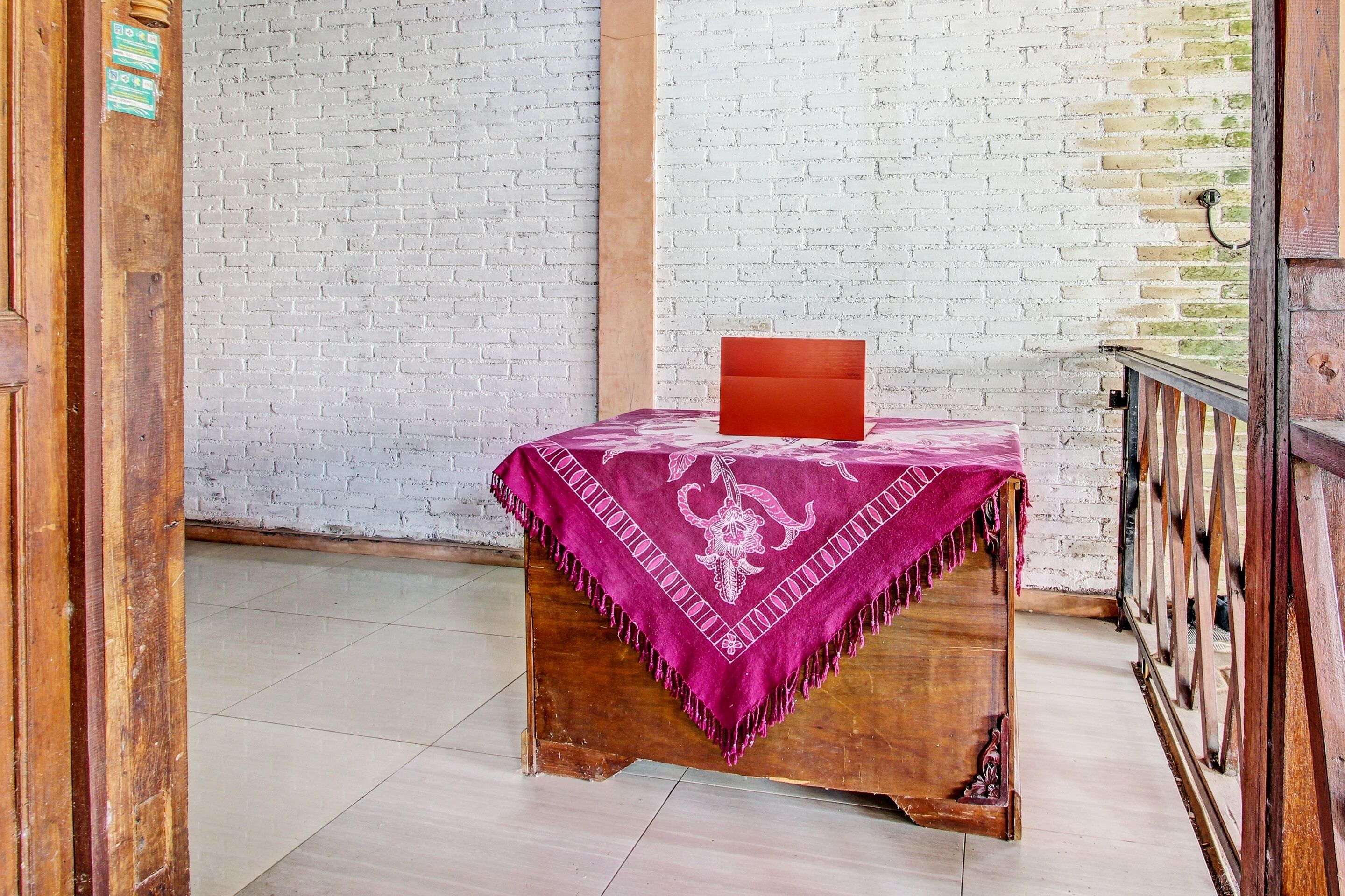 Una habitación con una mesa de madera cubierta por un paño morado, una pared de ladrillo blanco y una barandilla de madera.