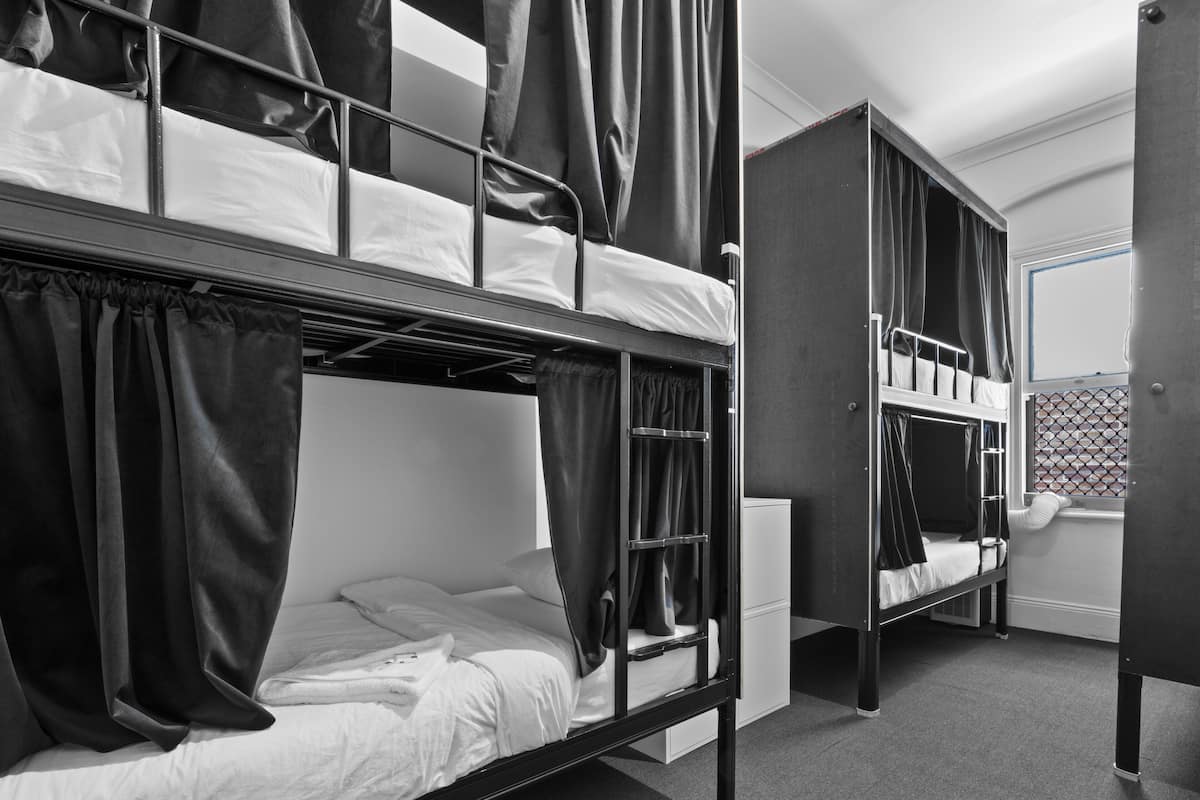 A dormitory-style room with bunk beds, a white wardrobe, and a window with a metal grid.