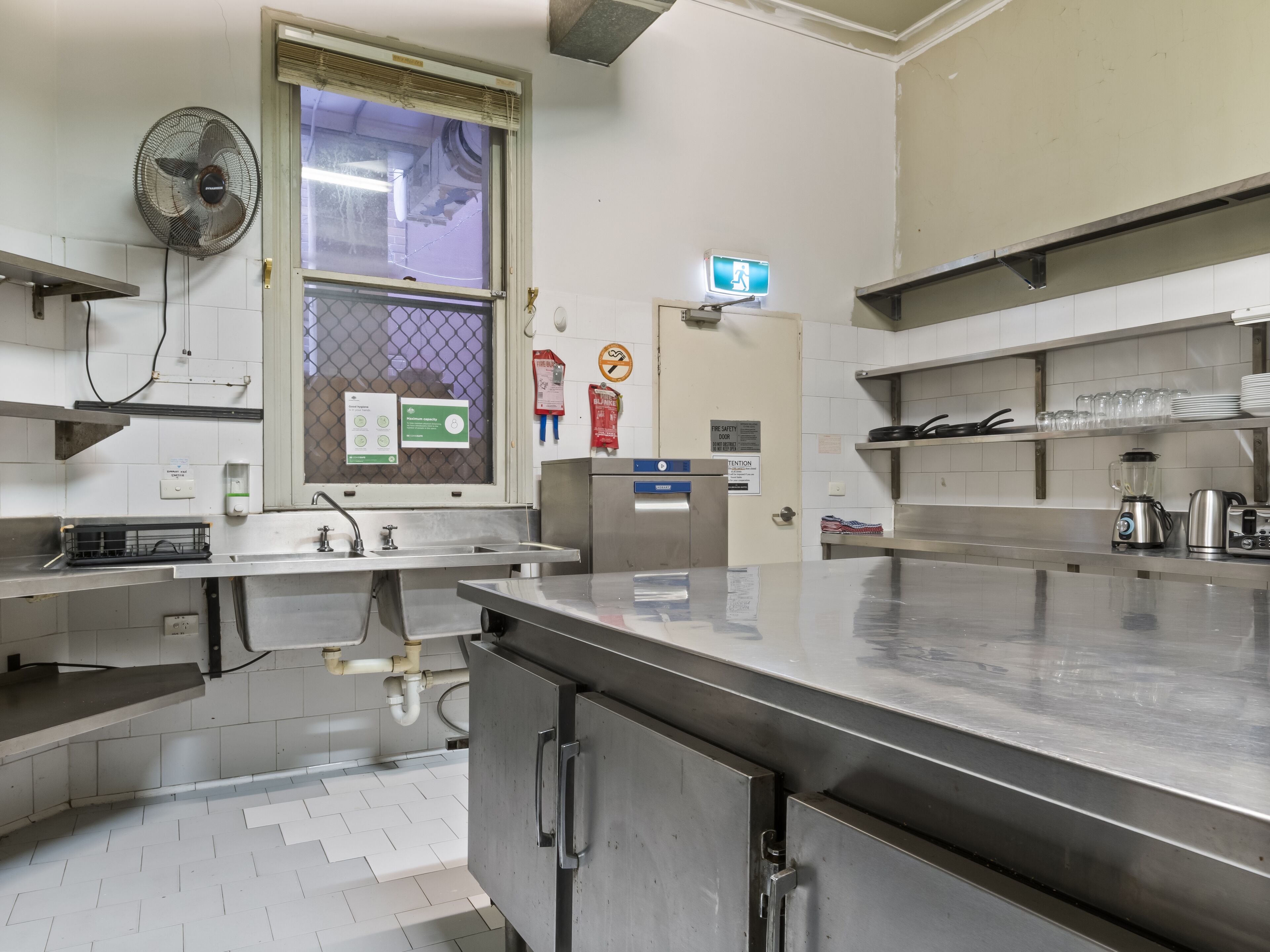 Een professionele keuken met roestvrijstalen werkbladen, een raam met ventilator en diverse keukenapparaten.