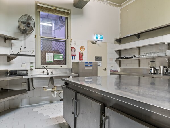 Una cocina comercial con mostradores de acero inoxidable, un ventanal con ventilador y diversos electrodomésticos.