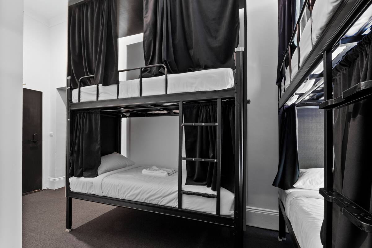 A bunk bed room with black metal frames, white bedding, and black curtains.