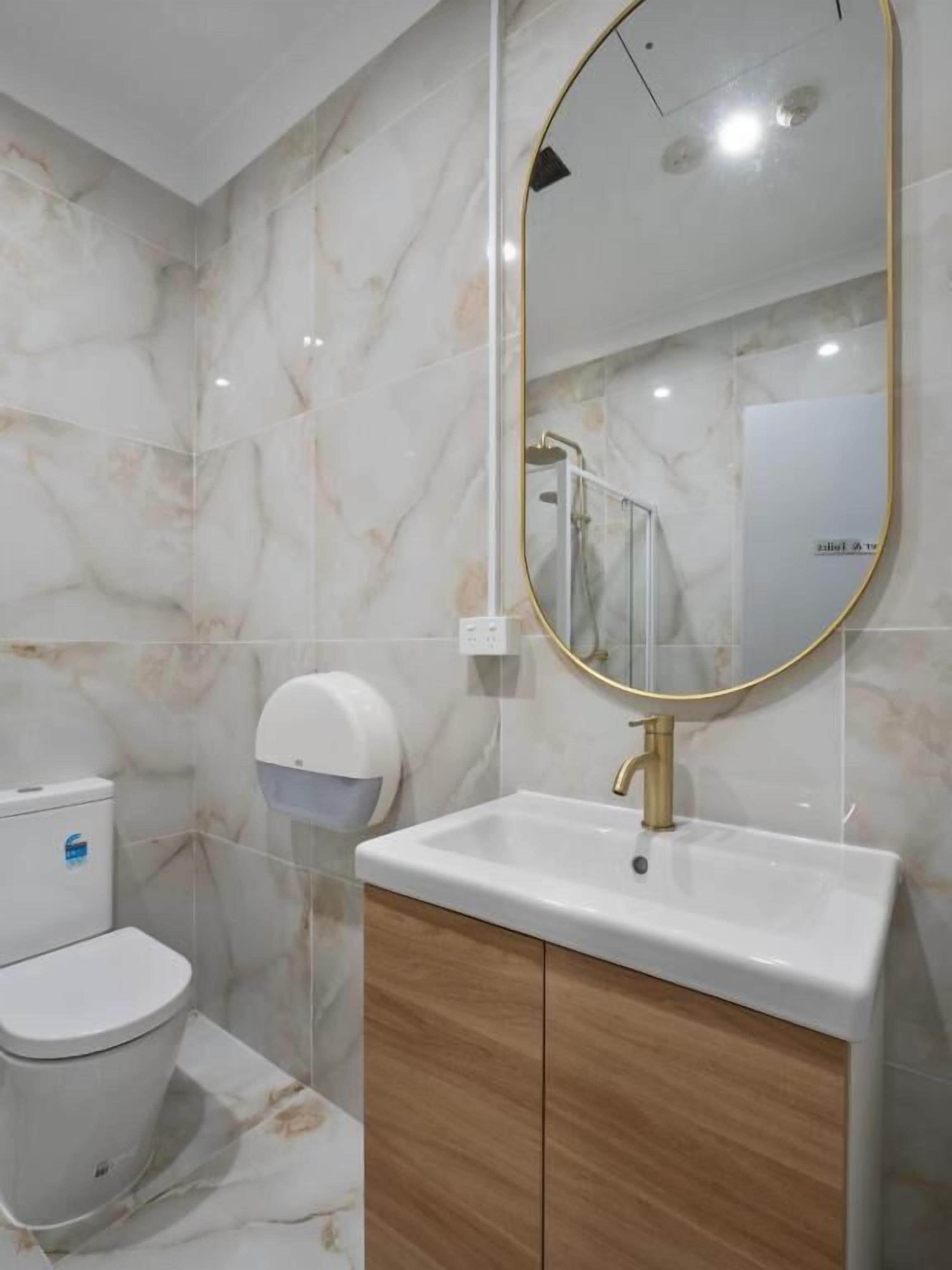 Ein modernes Badezimmer mit Marmorwand, Toilette, Waschbecken mit Goldarmatur und Spiegel mit Goldrahmen.