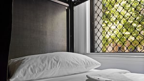 A neatly made bed with white linens and a white towel, a window with a metal screen, and a view of greenery outside. - Azzurro Pod Hotel Darling Harbour (Pyrmont)