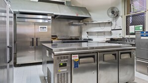 A commercial kitchen with stainless steel appliances, a ventilation hood, and a window with a view of greenery outside. - Azzurro Pod Hotel Darling Harbour (Pyrmont)