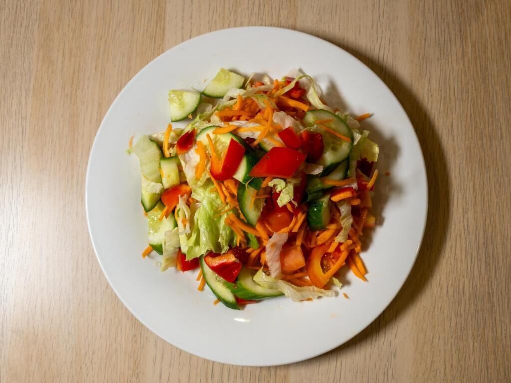 A white plate with a vegetable salad on a wooden table.