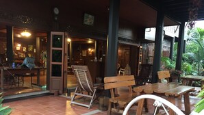 Un espacio interior con bancos y mesas de madera, suelo de baldosas y vistas al exterior a través de un acceso.