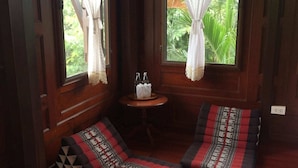 Una habitaci ón con dos zonas de estar acolchadas, una pequeña mesa redonda con una botella y pañuelos, y un ventanal con cortinas.