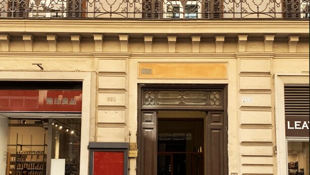 Une façade d’immeuble avec une entrée de magasin, un balcon orné de ferronnerie décorative et une enseigne portant le numéro 201.
