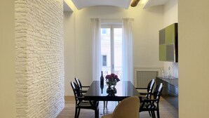 Un coin repas avec un mur en briques, une table avec des chaises, un vase de fleurs et une vue à travers une fenêtre avec des rideaux.