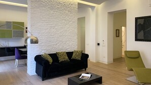 Un salon moderne avec un canapé noir, une table basse en verre et un mur blanc à texture.