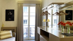 Une chambre d’hôtel avec un lit, un bureau doté d’une lampe, un miroir et une vue sur le balcon extérieur.