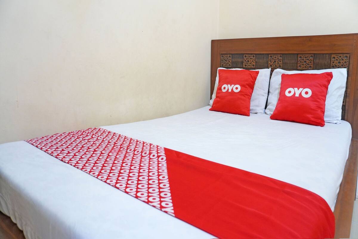 A bed with a white and red bedspread, two red pillows with the word "OYO" on them, and a wooden headboard with a decorative pattern.