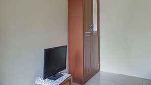 Een kamer met een televisie op een klein tafeltje, een hoge houten garderobe en een eenvoudige muur.