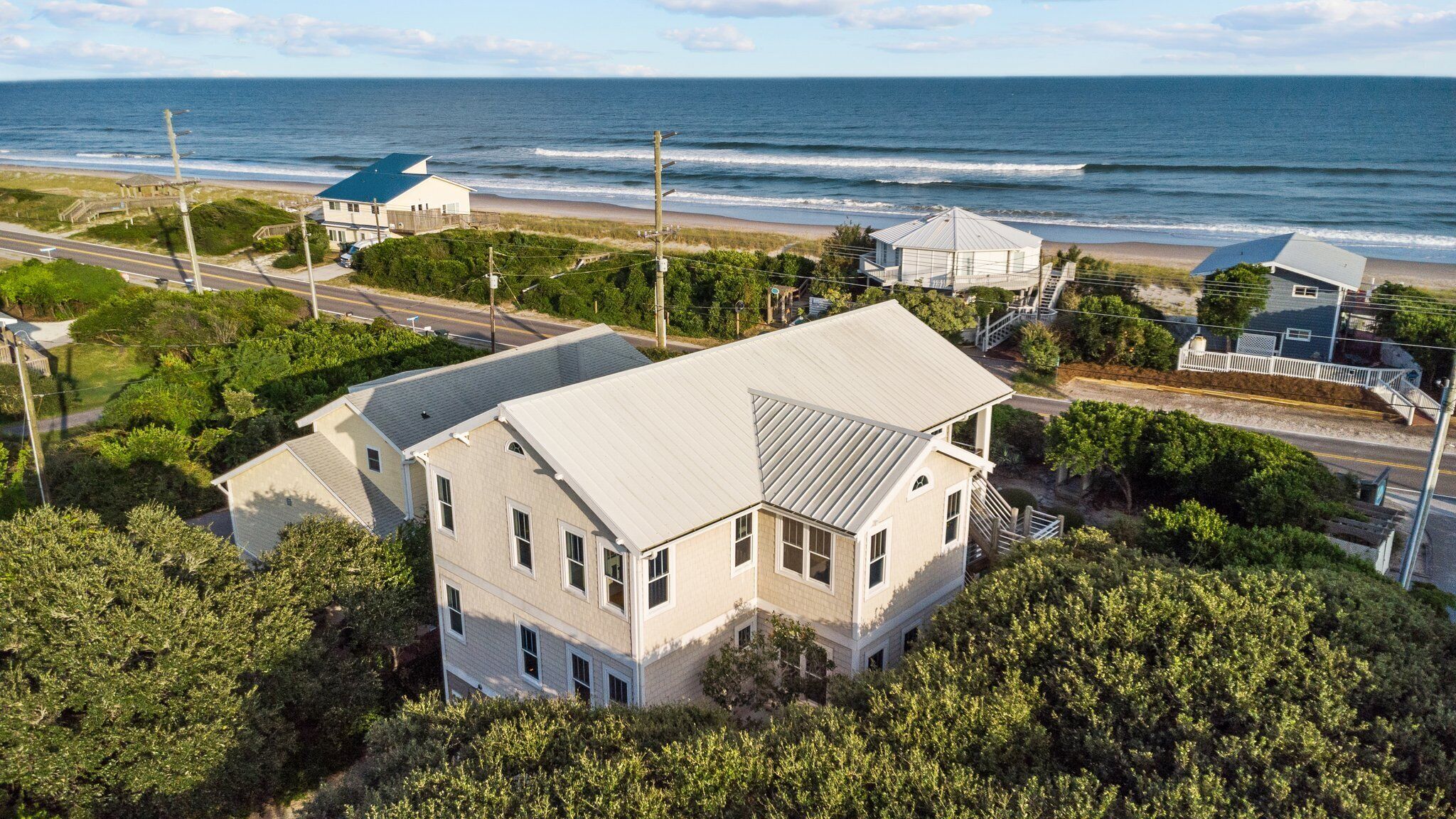 A coastal house with a large balcony, surrounded by dense greenery and a view of the ocean.