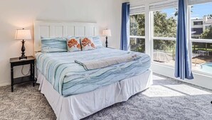 A bedroom with a bed, nightstands, lamps, and a view of an outdoor pool. - Tranquil Bay #50 (Rockport)