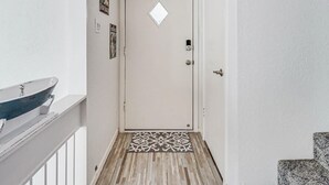 A hallway with a white door, a small window, a metal doorbell, and a patterned rug on the floor. - Tranquil Bay #50 (Rockport)