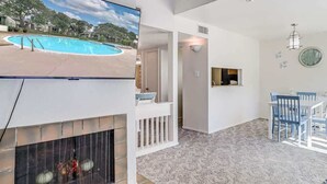 A living room with a fireplace, a pool view, a dining area, and a kitchen. - Tranquil Bay #50 (Rockport)