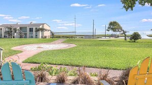 A grassy area with a pathway, a building, and a body of water in the background. - Tranquil Bay #50 (Rockport)