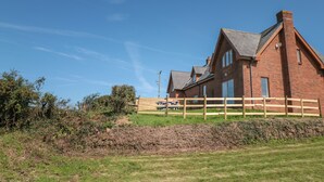 A large brick house with a sloped roof, a wooden fence, and a stone wall in the foreground. - Halls Farm (Bude)