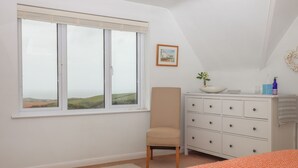 A bedroom with a bed, a dresser, a chair, a window with a view of the countryside, and a framed picture on the wall. - Halls Farm (Bude)