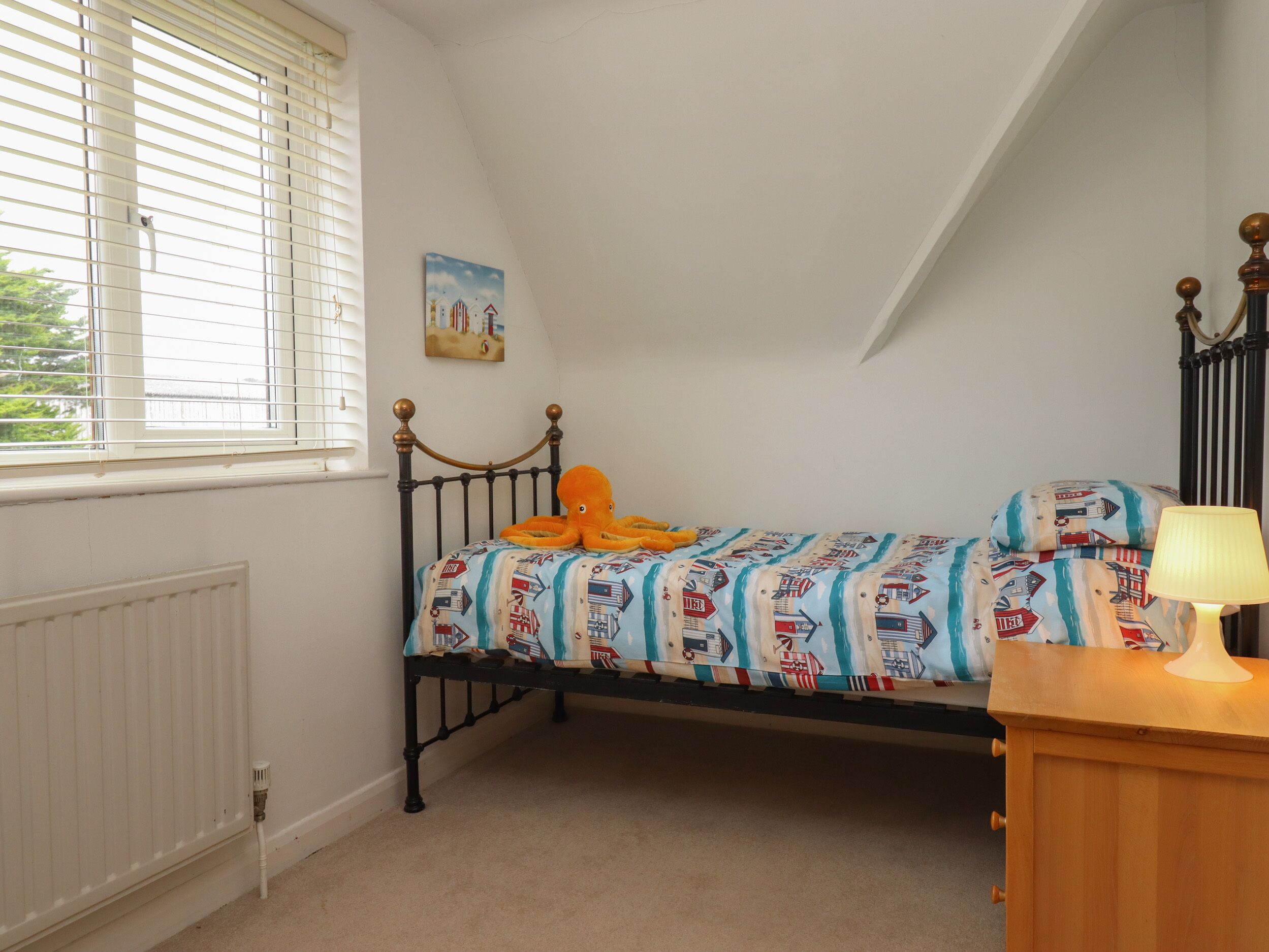 A bedroom with a single bed, a window with blinds, a radiator, a painting on the wall, and a lamp on a bedside table.