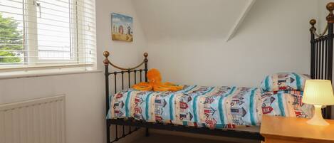 A bedroom with a single bed, a window with blinds, a radiator, a painting on the wall, and a lamp on a bedside table.