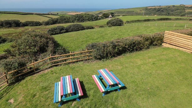 A grassy outdoor area with two colorful picnic tables and a wooden fence. - Halls Farm (Bude)