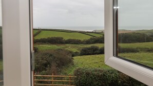 A view from a window overlooking a green landscape with fields and a distant coastline. - Halls Farm (Bude)