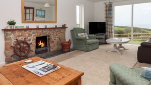 A living room with a stone fireplace, a television, and a view of the countryside. - Halls Farm (Bude)