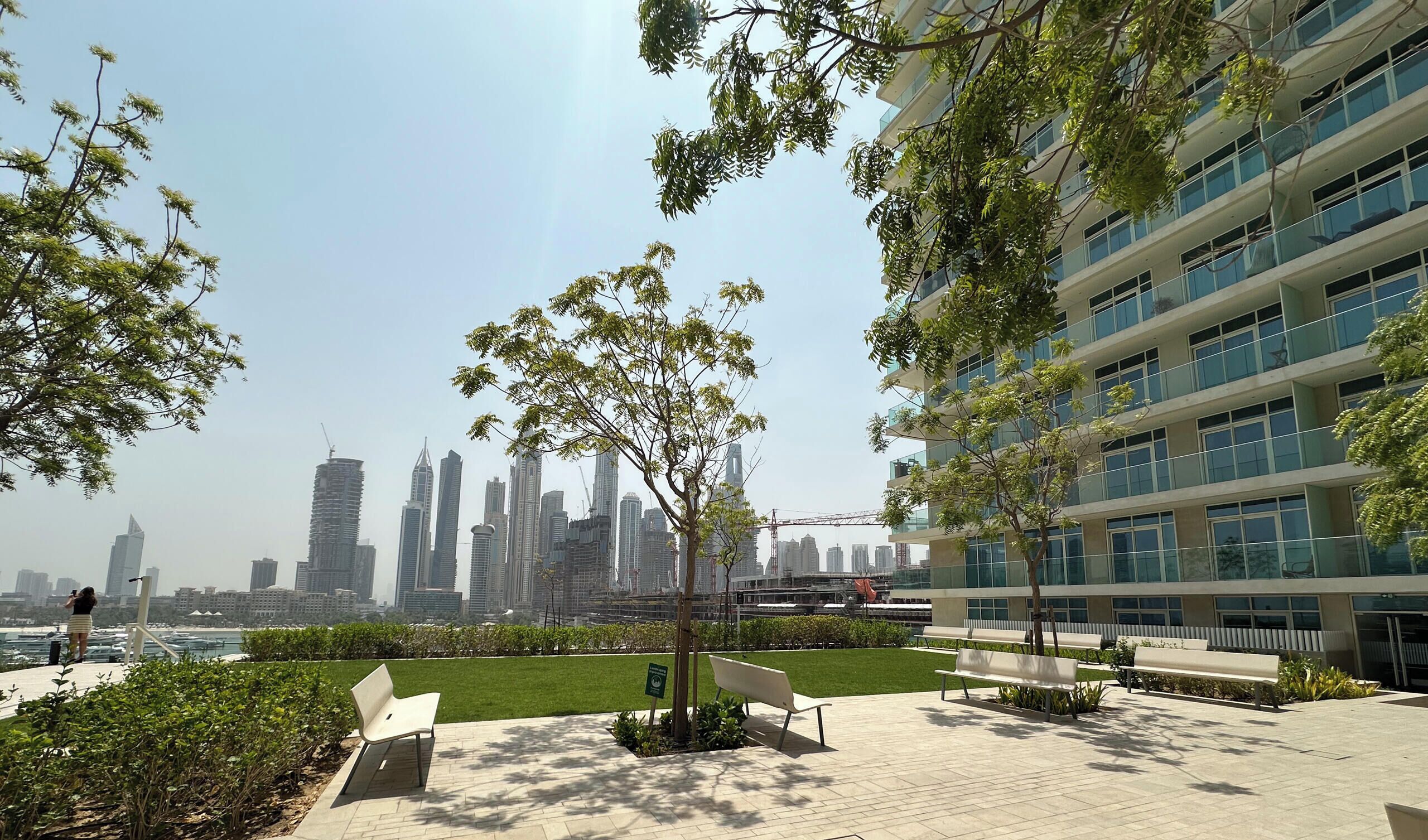 A modern urban park with a view of a city skyline, including high-rise buildings and a construction crane.