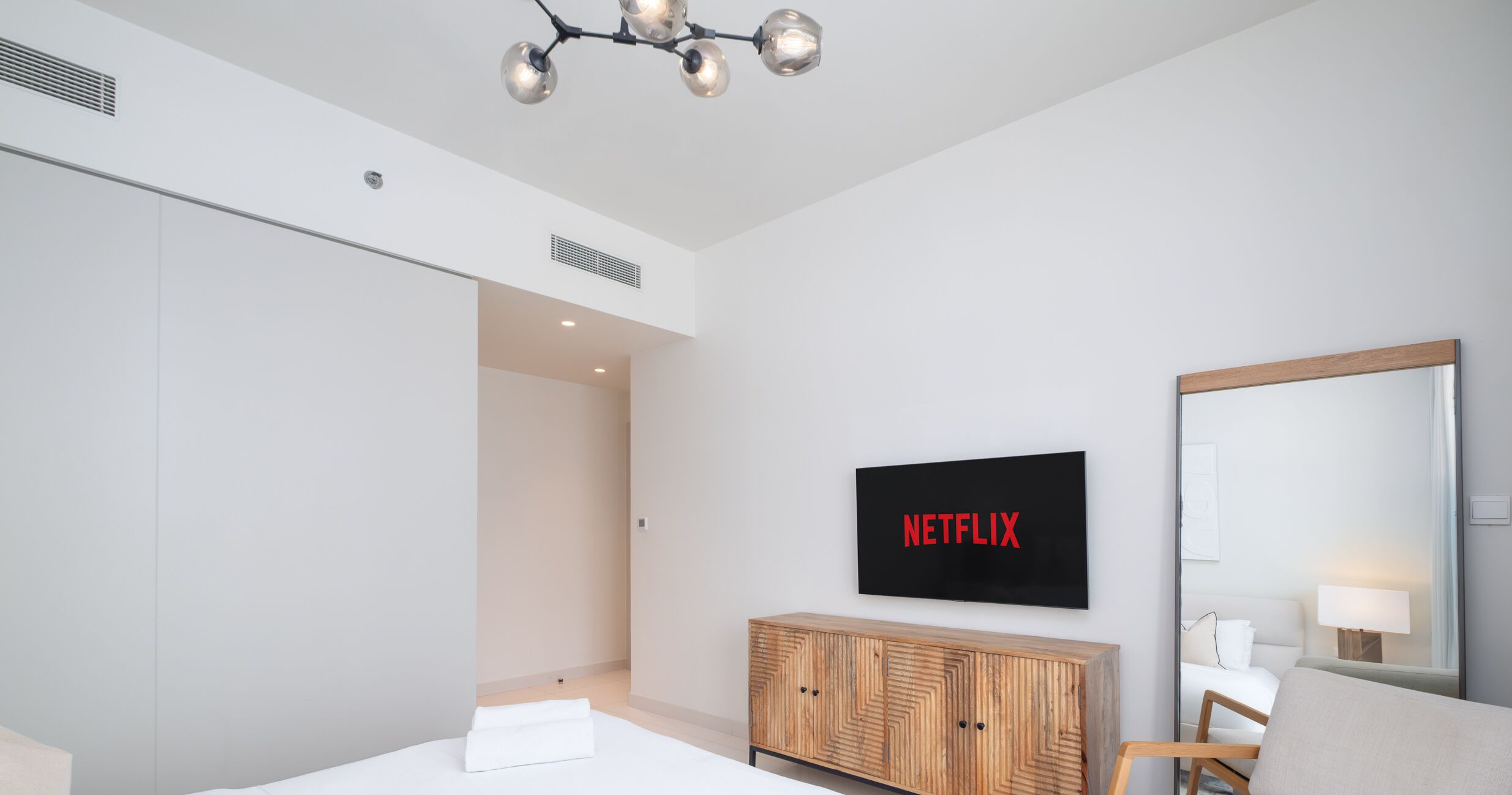 A modern hotel room with a large bed, a wooden cabinet, a TV mounted on the wall, and a mirror.