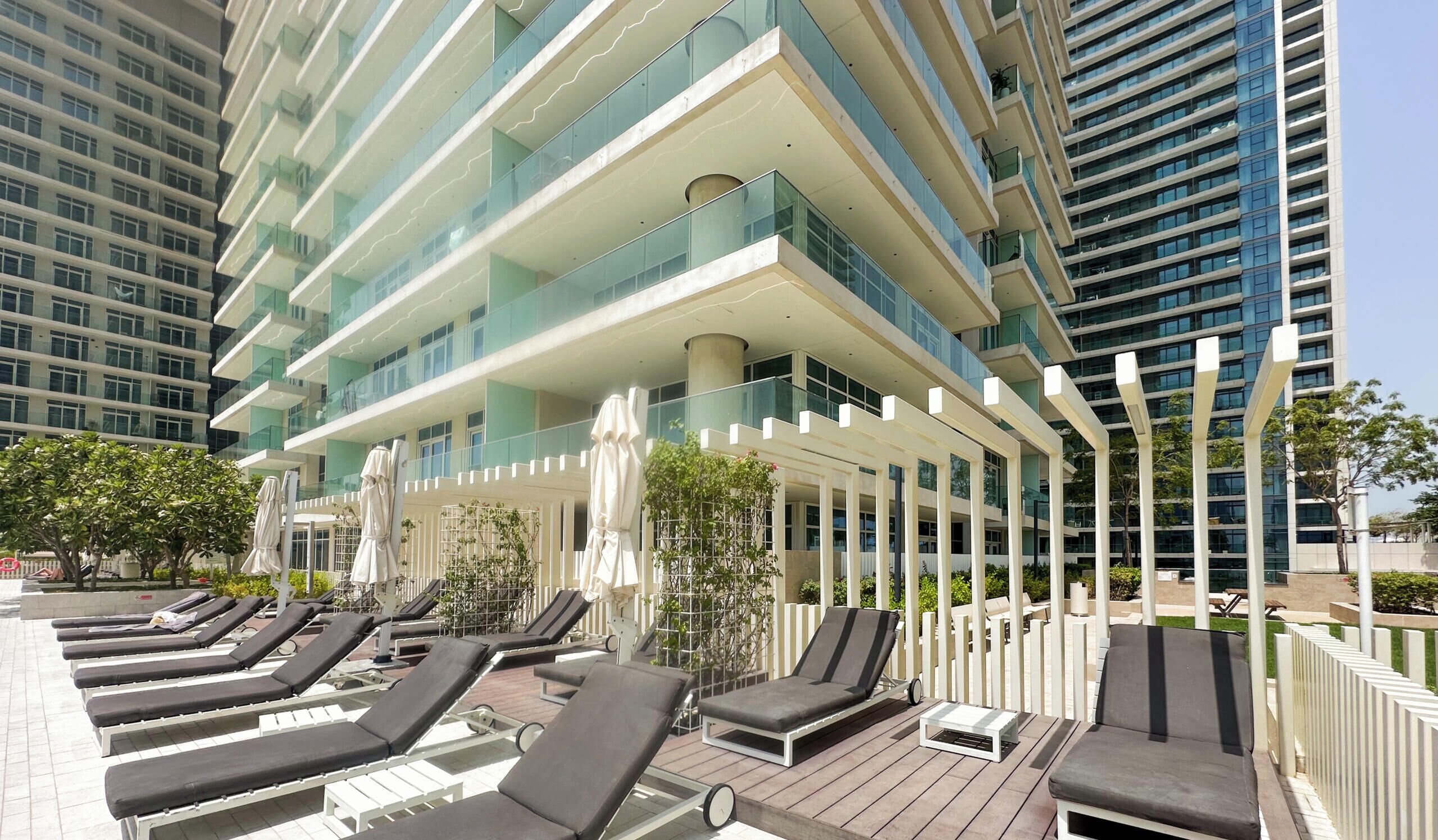A rooftop lounge area with sun loungers and umbrellas, surrounded by high-rise buildings.