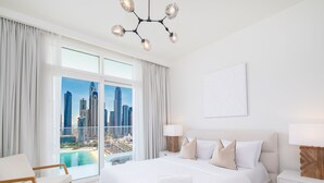 Une chambre d’hôtel avec un grand lit, deux tables de chevet, un lustre moderne, une vue sur la ville et un balcon avec une piscine.