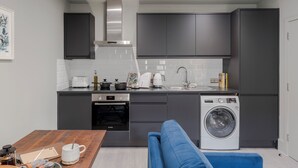 A compact kitchen with a washing machine, a toaster, and a coffee maker. - Your Apartment Tooting (London)