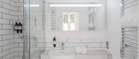 A modern bathroom with a glass-enclosed shower, a white sink, and a mirror above it.