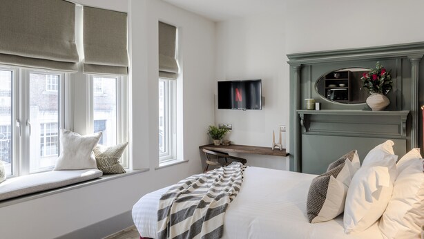 A bedroom with a bed, window seat, TV, and a green fireplace. - Your Apartment Tooting (London)