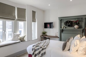 Une chambre à coucher avec un lit, un coin fenêtre, une télévision et une cheminée verte.