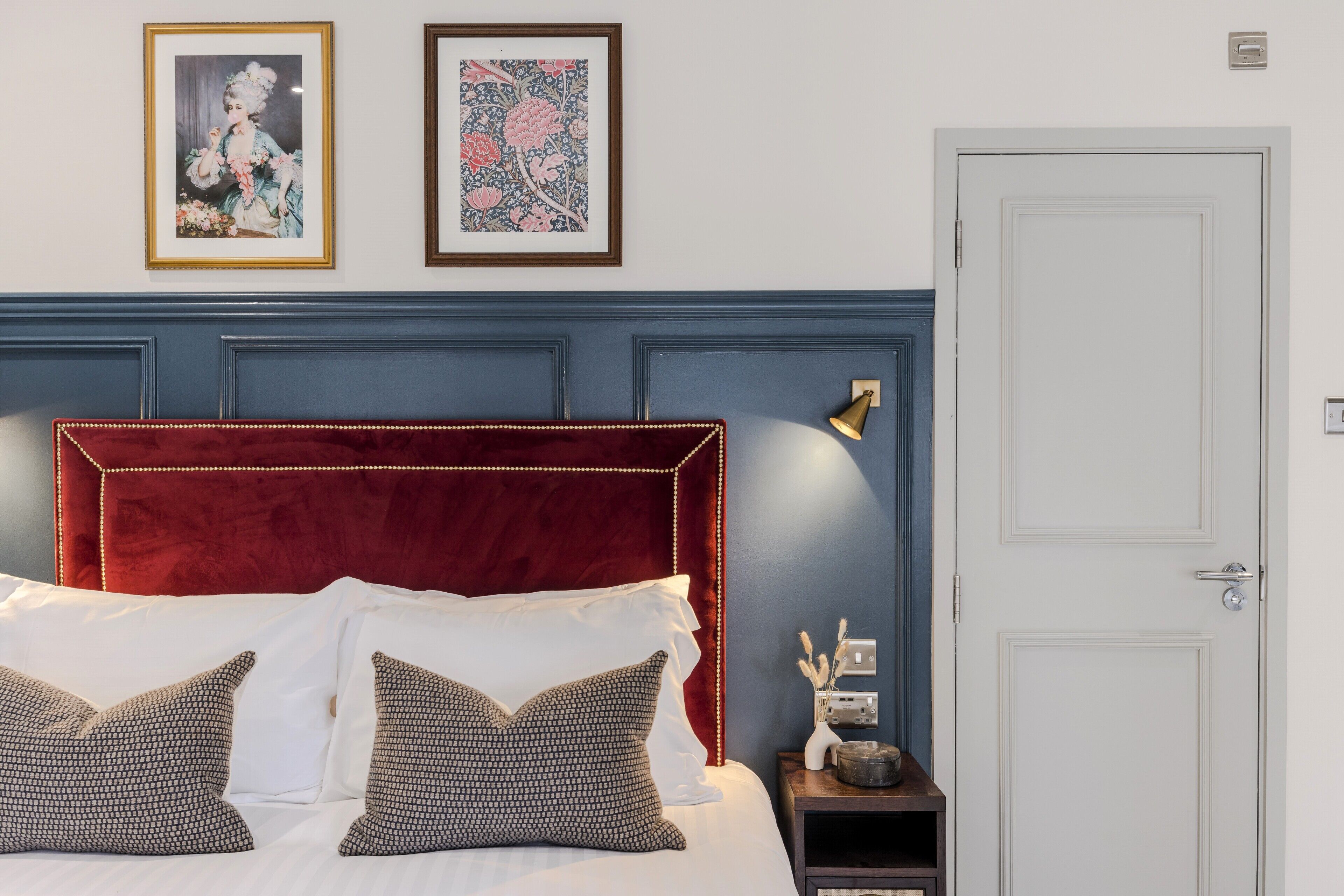A bedroom with a red upholstered headboard, white bedding, and two framed artworks on the wall.