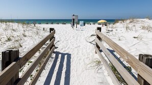 A sandy beach with a wooden walkway leading to the water, a signpost, and a yellow umbrella.