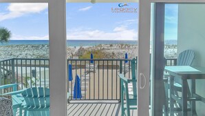 A balcony with a view of the beach, a table, chairs, and a sign for Legacy Vacations.