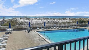 A pool area with lounge chairs and umbrellas, overlooking a beach with sand dunes and the ocean.