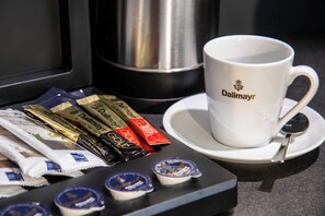 Una taza de café con el logo 'Dalmayr' sobre un plato, una cuchara y varios paquetes de café en una bandeja.