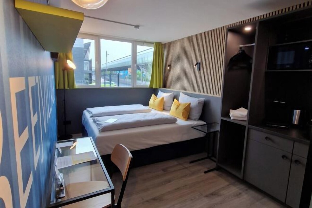A modern hotel room with a bed, a desk, and a wardrobe.