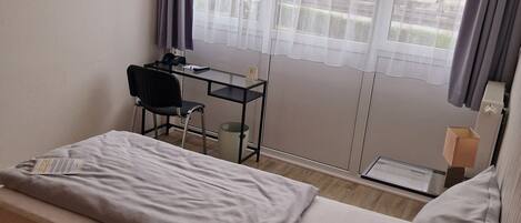 A single-bed room with a desk, chair, and a TV mounted on the wall.